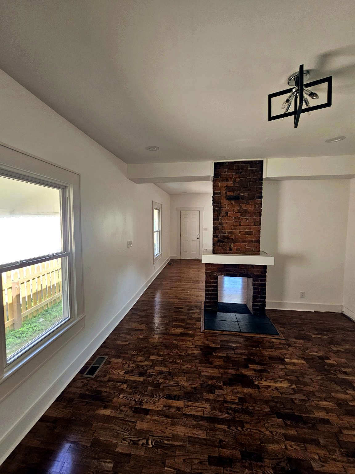 Finished living room with exposed brick fireplace and refinished hardwood floors